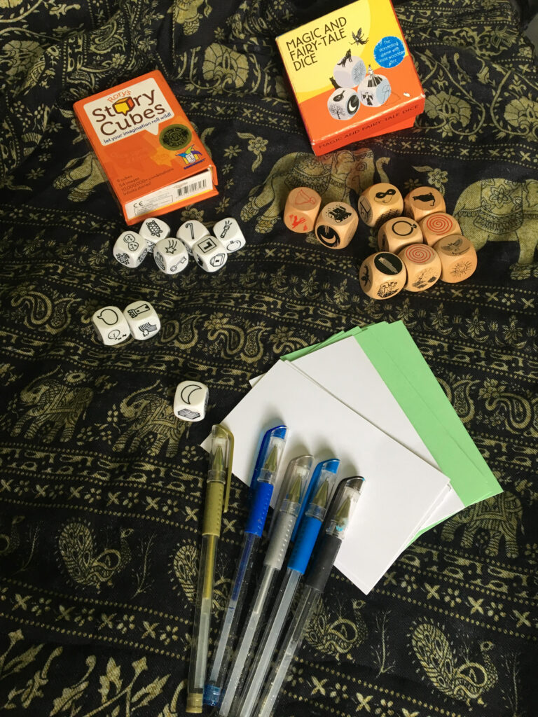 storytelling dice, index cards, and pens resting on a patterned scarf